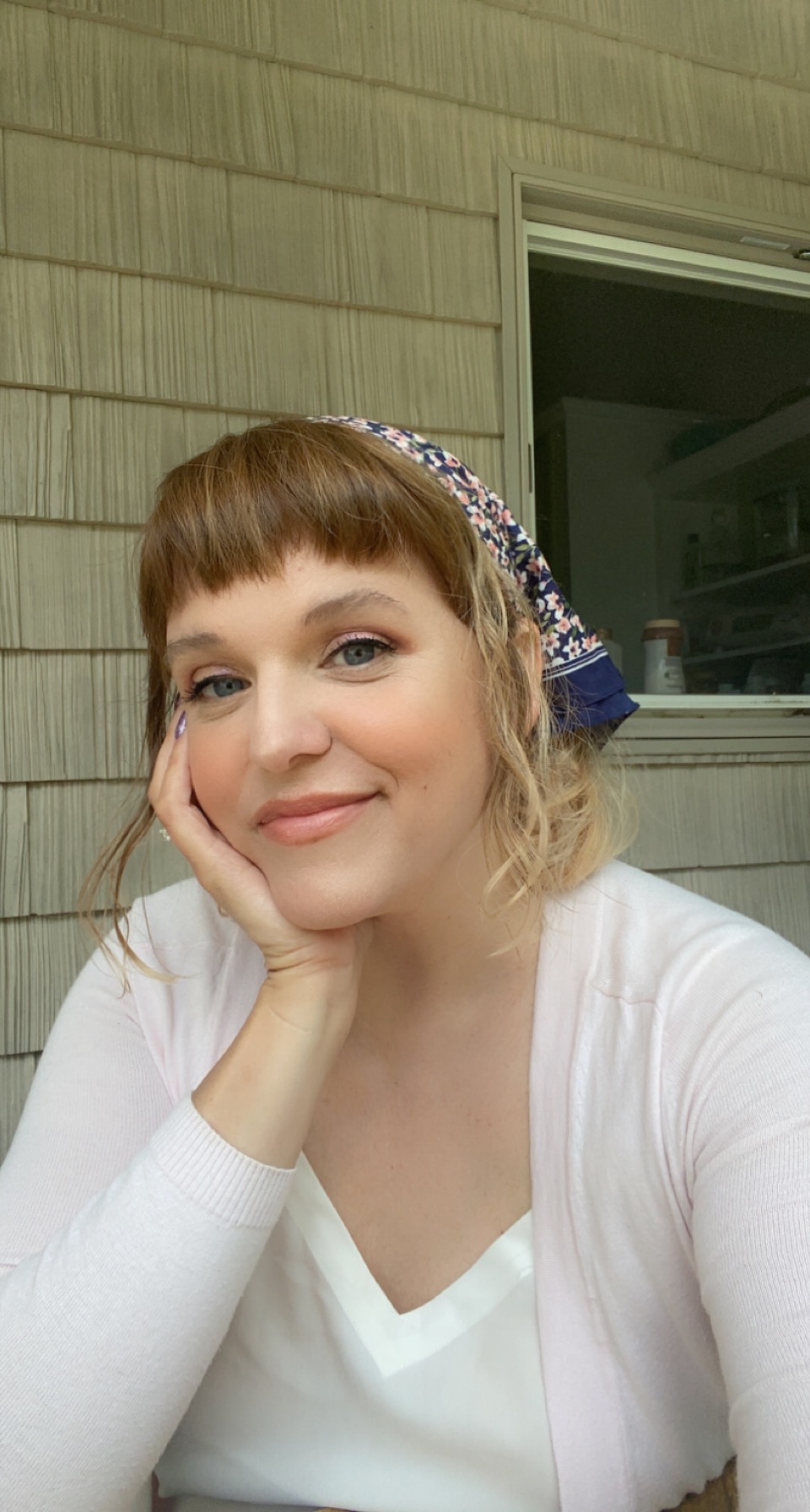 Libby looks at the camera with a smile on her face, resting her face on her hand. Her nails are metallic purple and her hair is pulled back in a bandana.